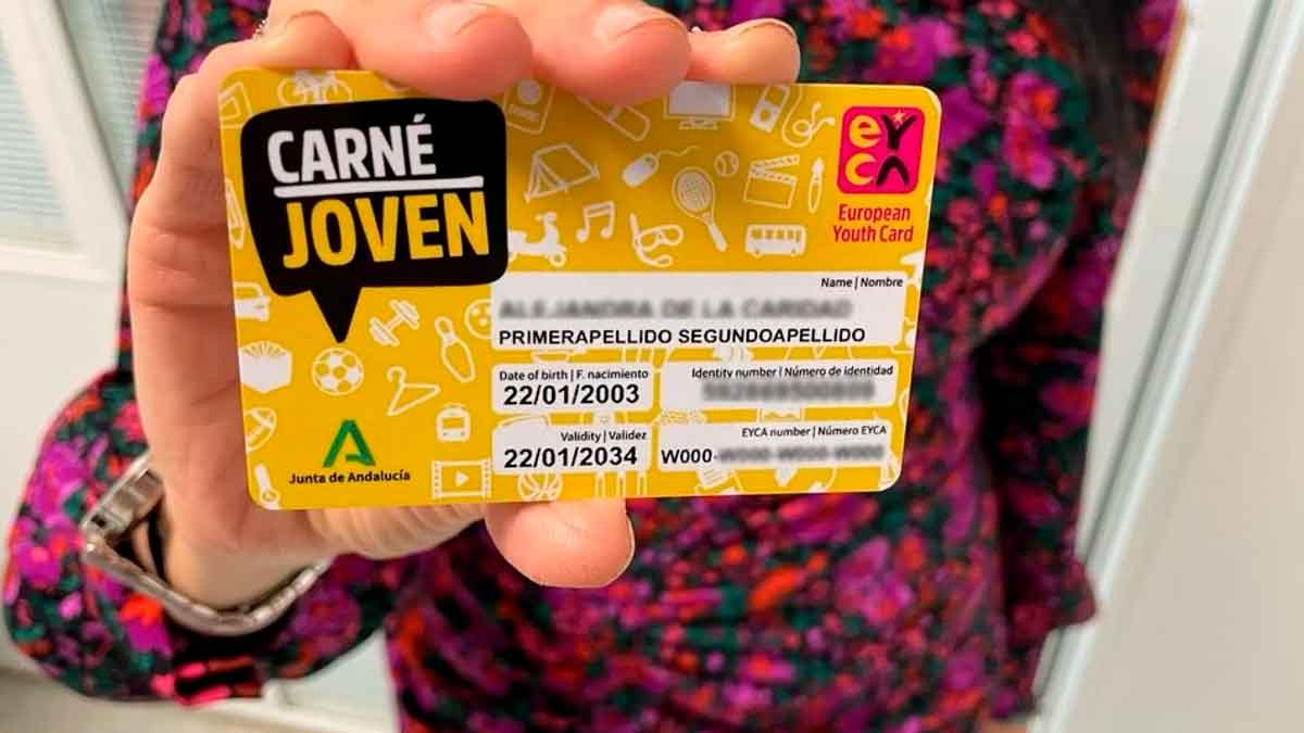 Carné Joven Andalucía tarjeta amarilla con descuentos, sostenida por una joven ante fondo colorido