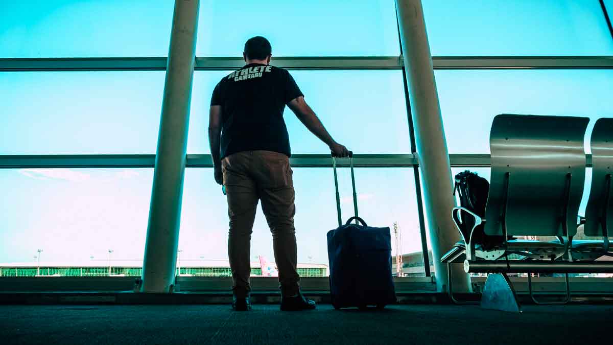 Hombre desempleado con maleta en un aeropuerto, a punto de viajar, arriesgando perder la prestación por desempleo del SEPE por no notificar la salida