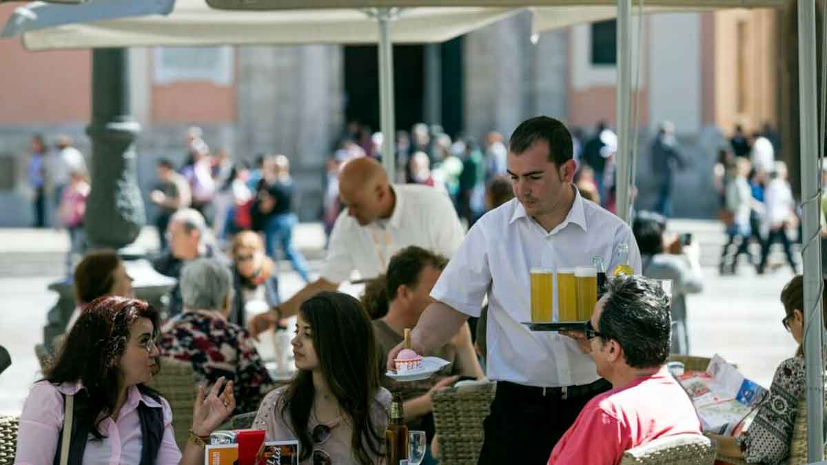 Camarero sirviendo bebidas a clientes en la terraza de un bar, ejemplo de empleo precario en la hostelería española