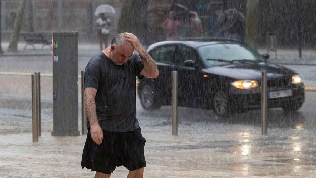Hombre caminando bajo fuerte lluvia en Granada durante las tormentas y reventones anunciados por la AEMET en plena ola de calor