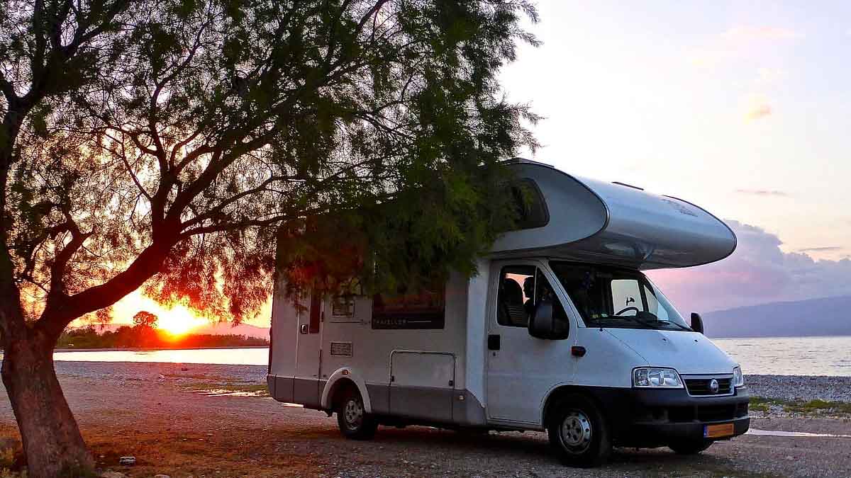 Autocaravana blanca aparcada junto al mar al atardecer, ejemplo de viaje en caravana siguiendo las normas DGT para evitar multas