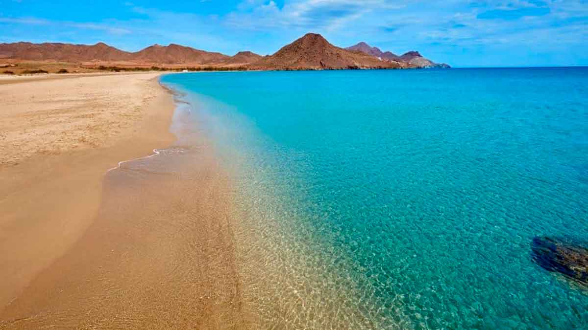 Playa andaluza de arena fina y aguas cristalinas en un entorno natural con montañas al fondo