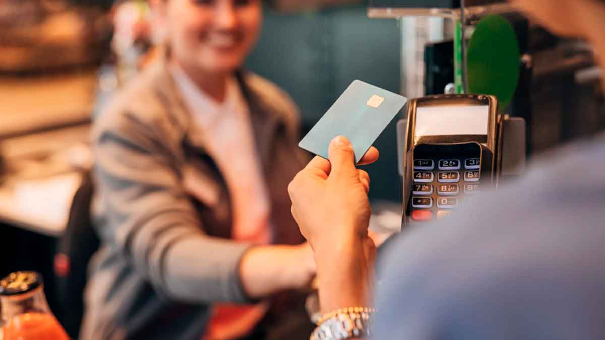 Persona paga con tarjeta en un comercio mientras la dependienta atiende la operación