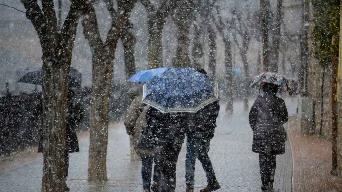 Personas caminando bajo lluvia y frío intenso con paraguas en una avenida durante un episodio invernal