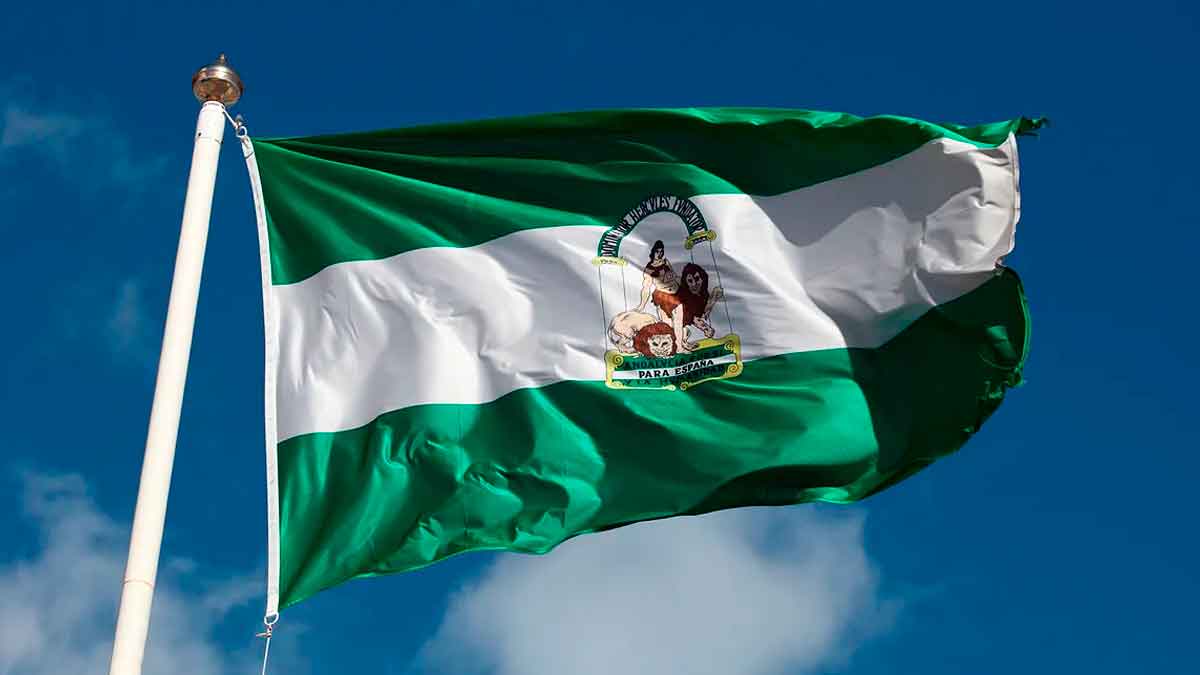 Bandera de Andalucía ondeando al viento sobre un cielo azul