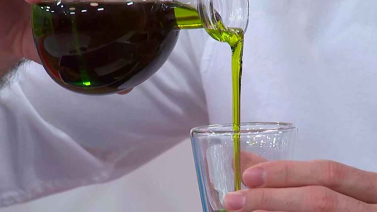 AOVE de cosecha temprana vertiéndose en un vaso, con color verde intenso y aspecto fresco