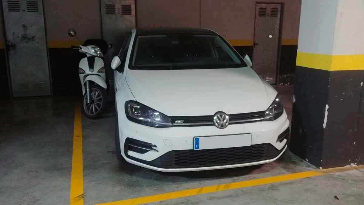 Coche y moto aparcados en la misma plaza de garaje comunitario delimitada con líneas amarillas
