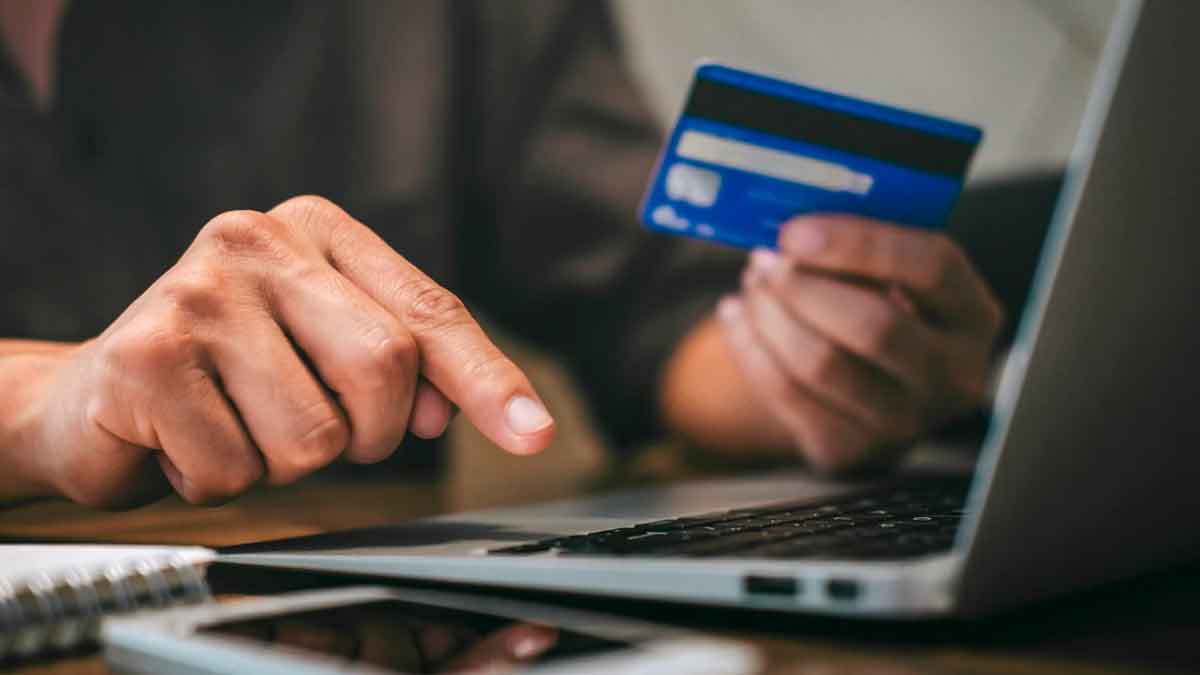 Persona usando una tarjeta bancaria para pagar por Internet en un ordenador portátil