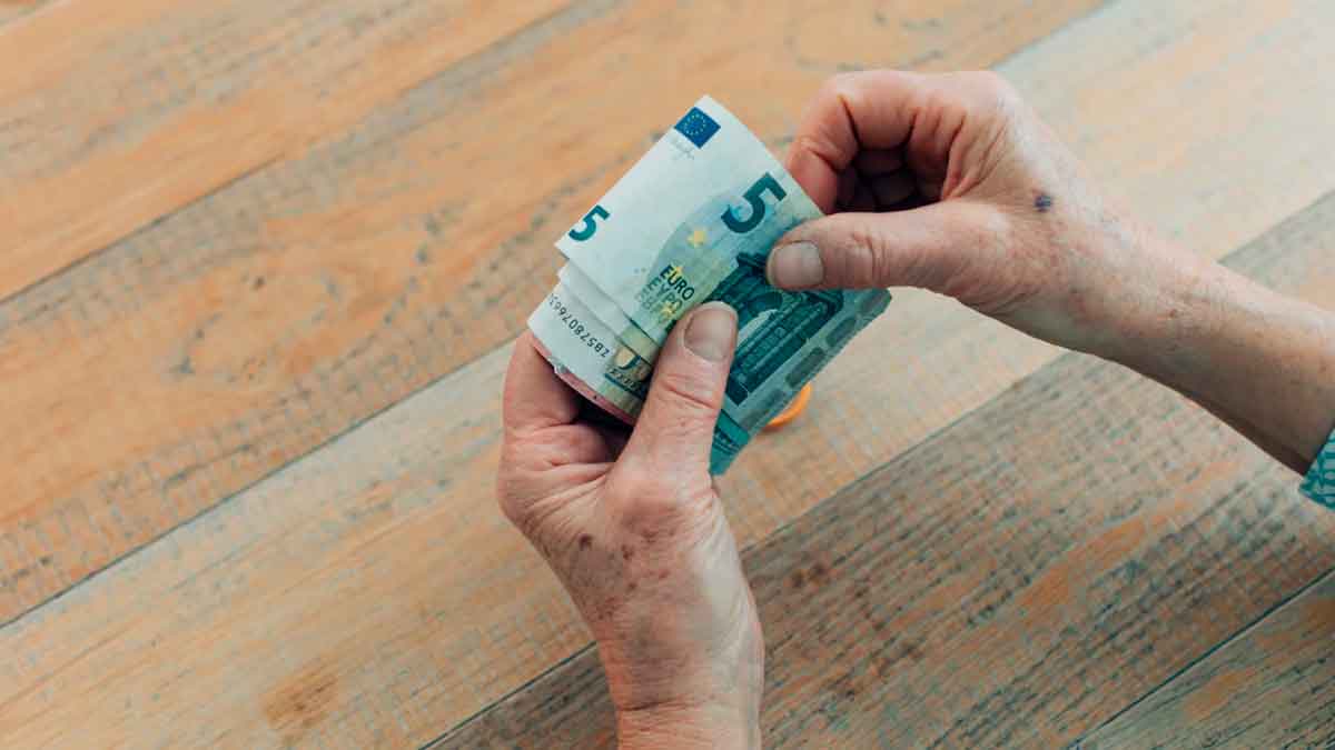Persona mayor contando billetes de euro relacionados con la pensión media en 2026 y la edad de jubilación