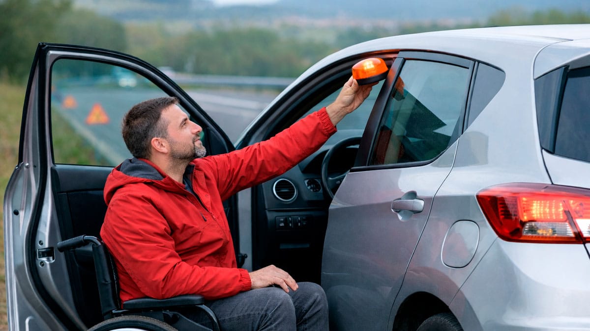 Conductor con discapacidad colocando la baliza V-16 en la puerta del coche tras una avería en carretera