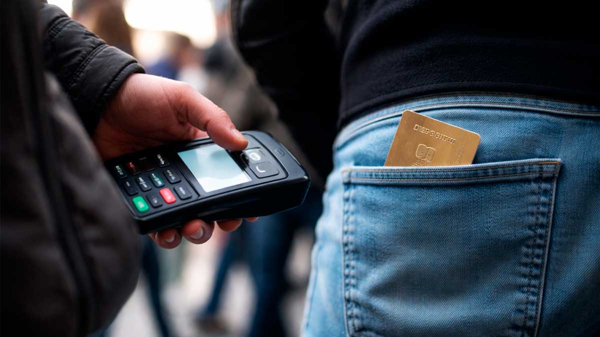 Hombre con datáfono portátil acercándolo al bolsillo trasero con tarjeta contactless para ilustrar el ghost tapping