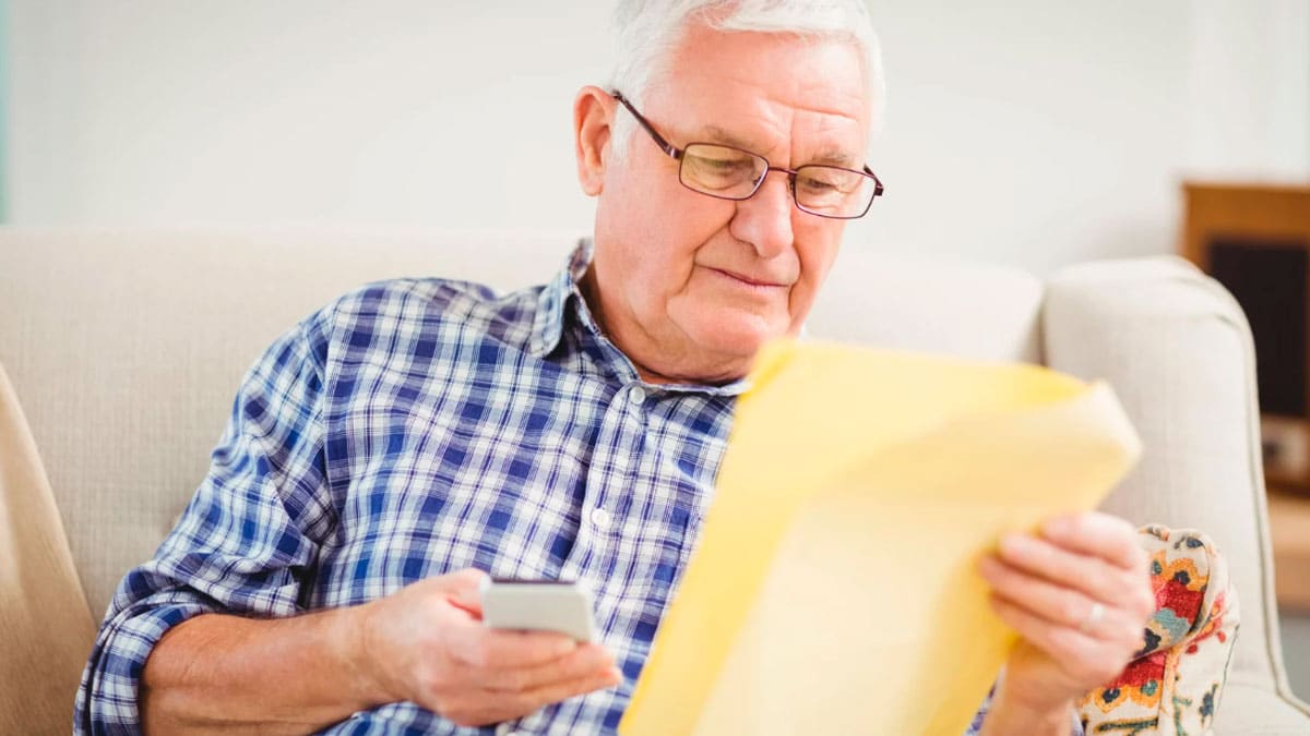 Pensionista revisa una carta de Hacienda mientras consulta su móvil por la devolución del IRPF como mutualista