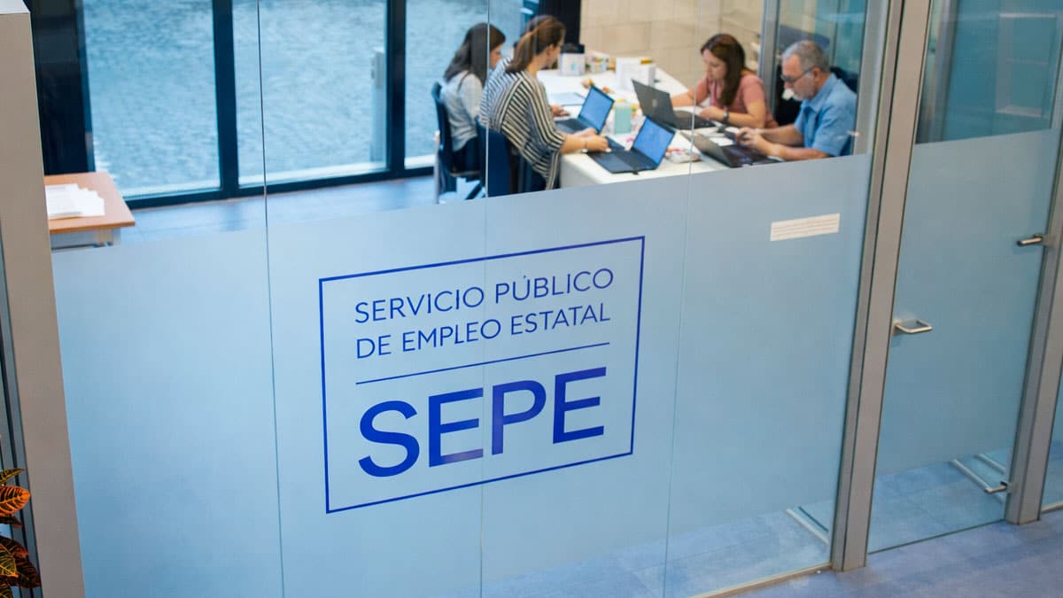 Oficina del SEPE con logotipo en cristal y trabajadores gestionando prestaciones por desempleo y el CAE