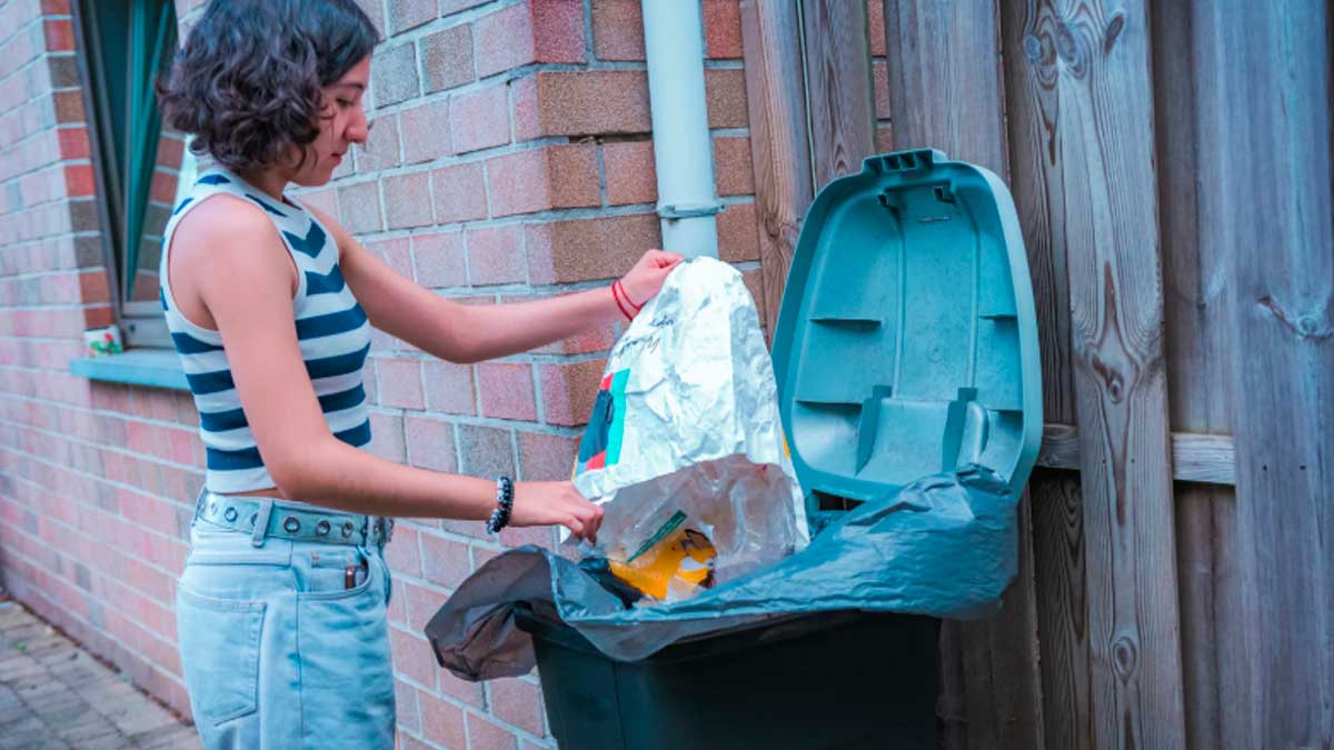 Mujer tirando residuos en cubo de basura para reducir desperdicio en el hogar