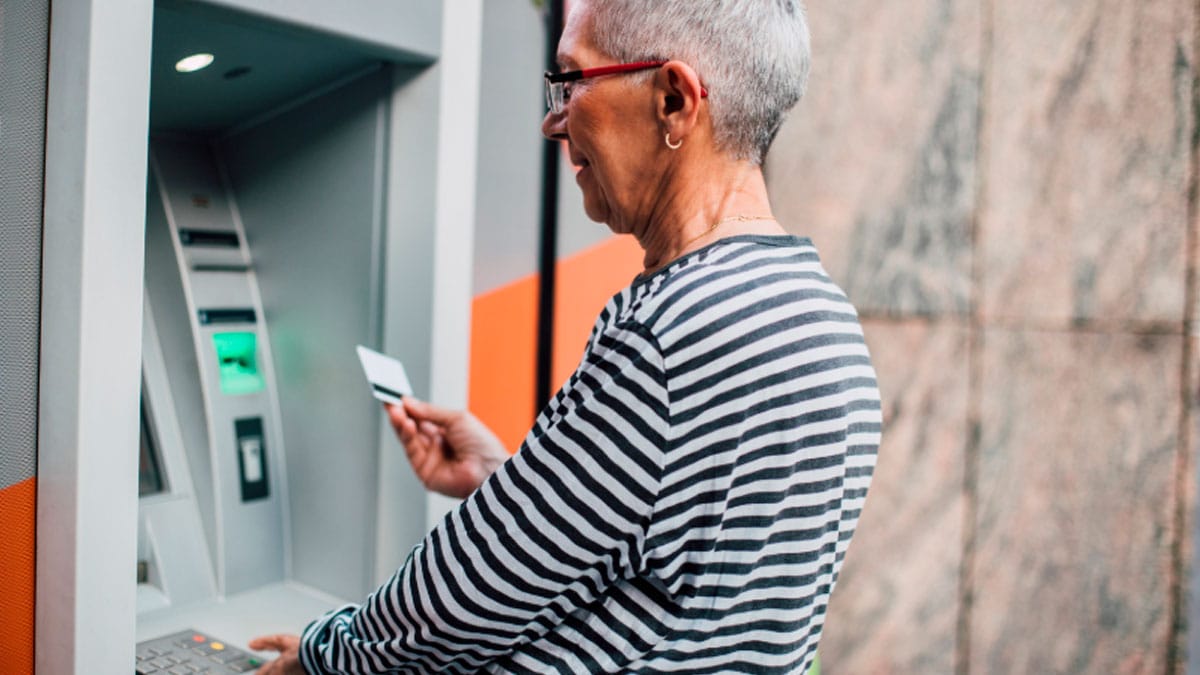 Pensionista retirando dinero en un cajero automático tras el ingreso de la pensión mensual.