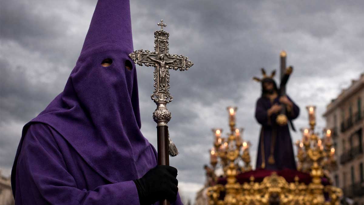 Nazareno en procesión de Semana Santa bajo cielo gris en Andalucía durante previsión de lluvias según AEMET