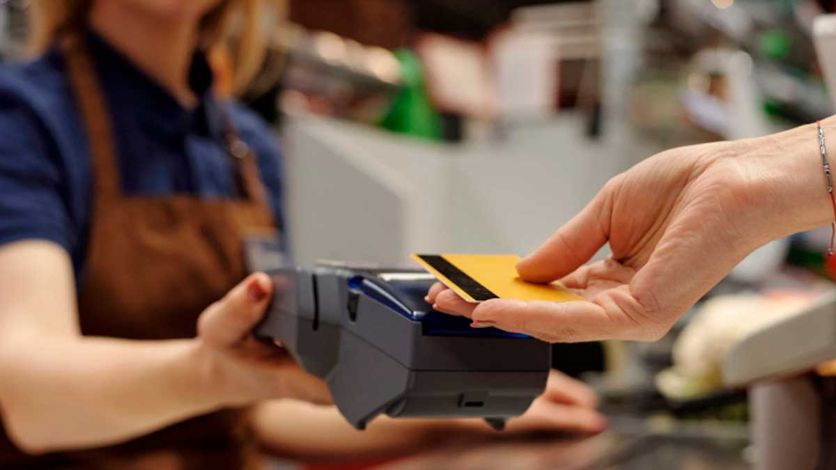 Persona pagando con tarjeta bancaria en un datáfono mientras expertos explican las diferencias entre débito y crédito