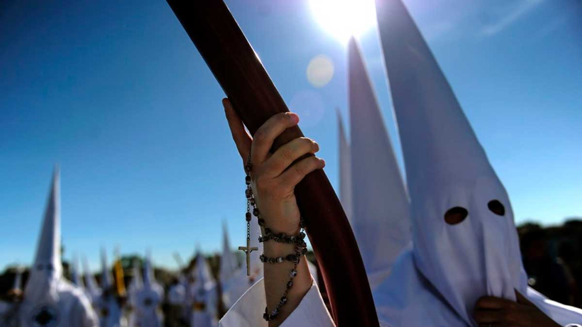 Nazarenos en procesión de Semana Santa en Andalucía bajo un cielo despejado y sol intenso