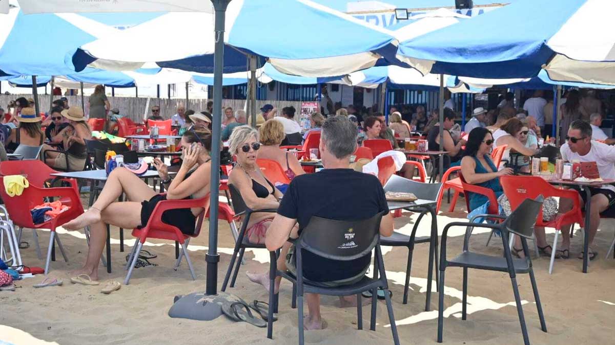 Clientes en terraza de bar en la playa bajo sombrillas durante un día de calor en Andalucía