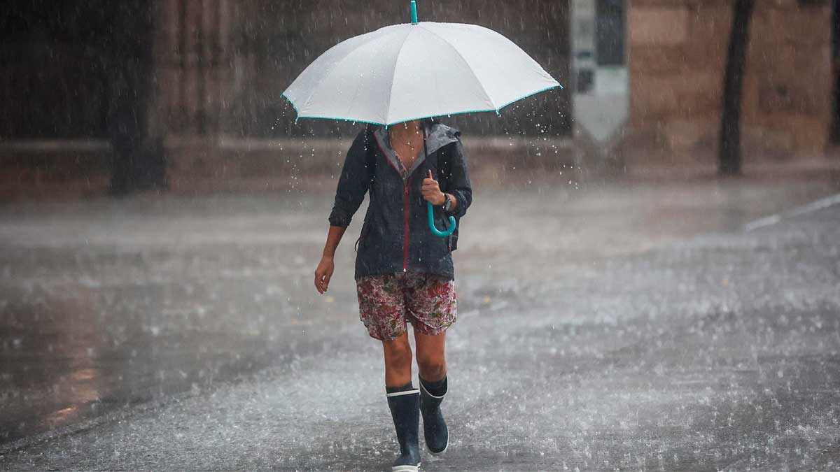 Persona caminando bajo la lluvia intensa con paraguas durante un episodio de tormentas en Andalucía