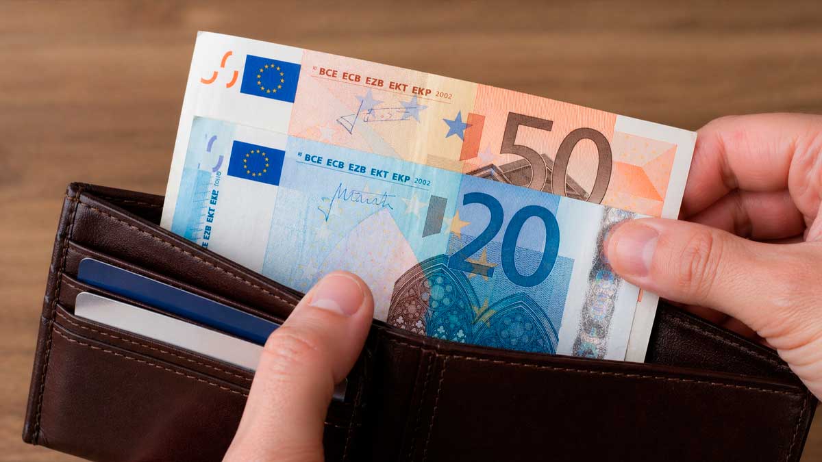 Manos sacando 70 euros en billetes de una cartera como recomendación del Banco de España para emergencias