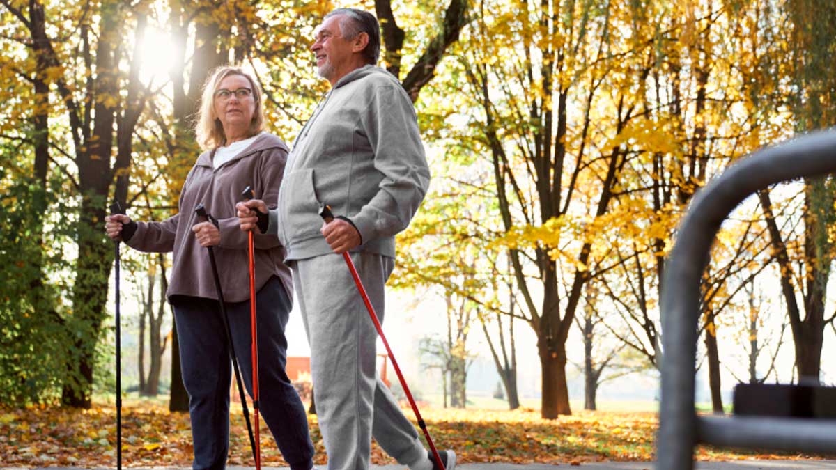 Pareja de personas mayores caminando con bastones en parque quemando calorías y mejorando su salud