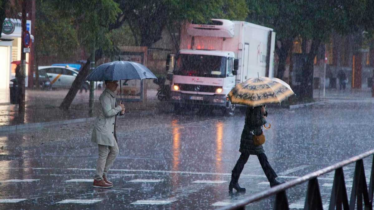Peatones cruzando bajo lluvia intensa en Andalucía durante una DANA con tormentas y chubascos