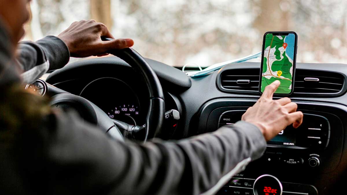 Conductor usando móvil en soporte mientras conduce con GPS en pantalla