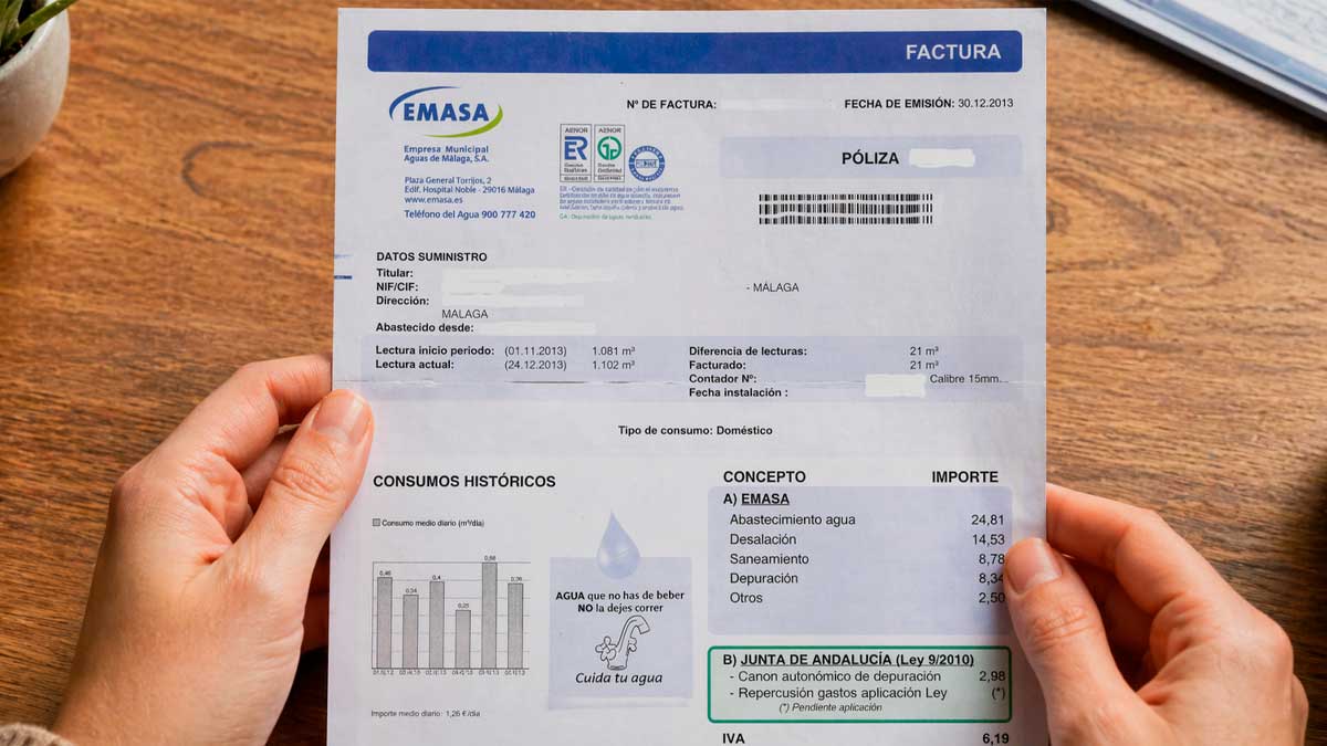 Factura de Emasa sostenida por un cliente con detalle de consumo y cargos en Málaga