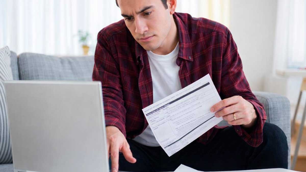 Hombre revisando la declaración de la renta 2025 en el ordenador con documentos fiscales en casa