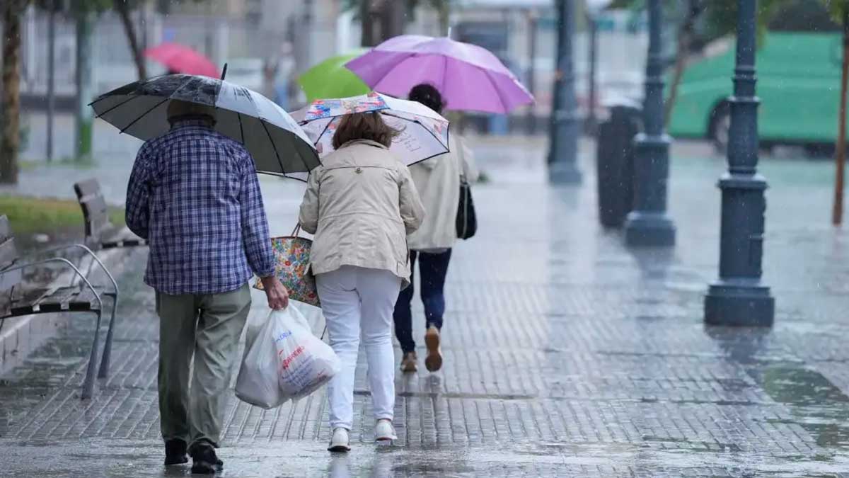 Personas caminando bajo la lluvia con paraguas en Andalucía durante un episodio de inestabilidad y tormentas