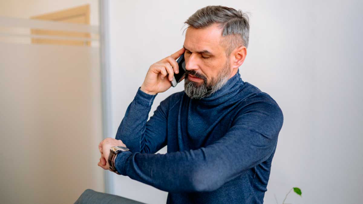Hombre consultando el reloj mientras habla por teléfono fuera de su horario laboral
