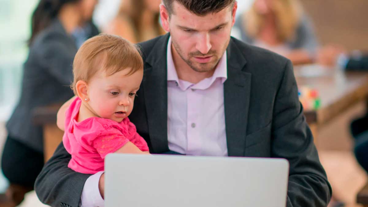 Padre trabajando con portátil mientras cuida a su hija conciliación laboral jornada flexible