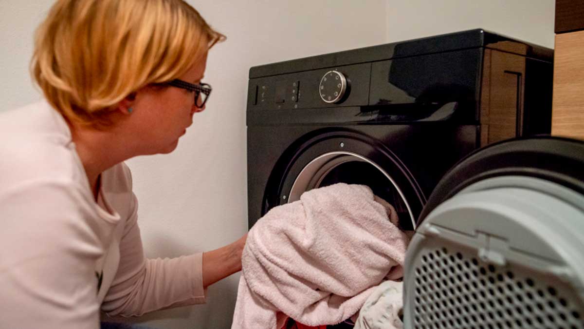 Mujer metiendo ropa en la lavadora por la noche en casa