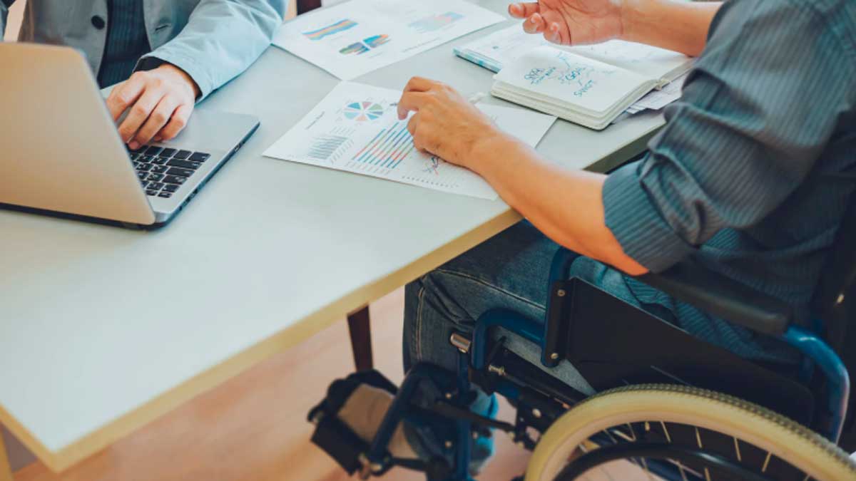 Persona en silla de ruedas trabajando en oficina con documentos y ordenador en Andalucía