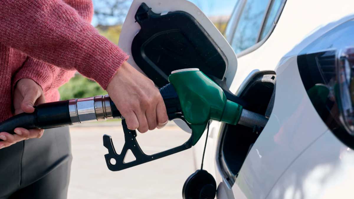 Persona repostando gasolina en un vehículo con surtidor verde en una gasolinera.