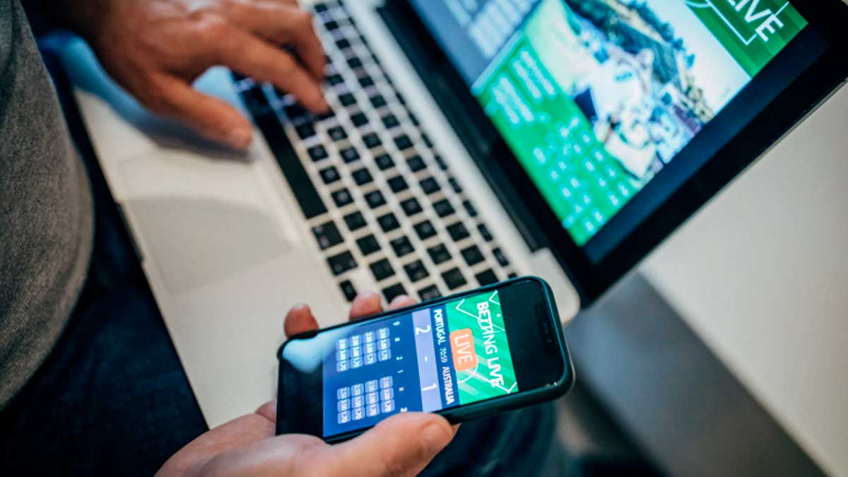 Usuario viendo fútbol pirata en móvil mientras navega en portátil con riesgo bloqueo de internet