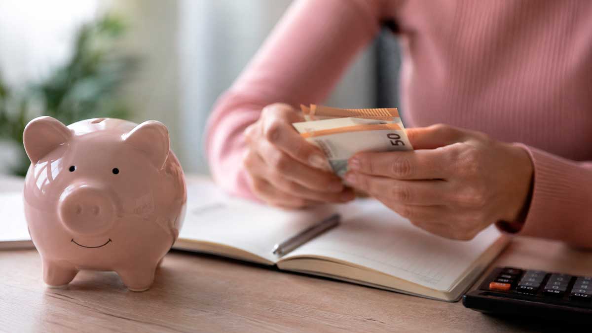 Persona contando billetes junto a una hucha para ahorrar dinero con cuentas remuneradas sin comisiones