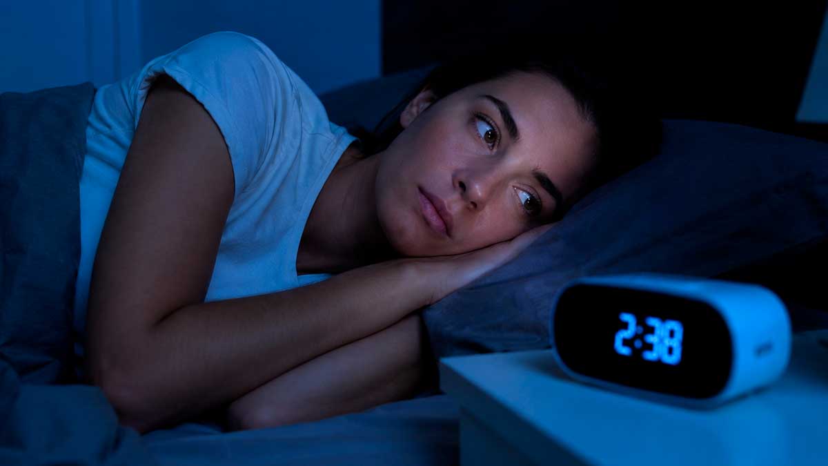 Mujer despierta mirando el reloj de madrugada por problemas de sueño