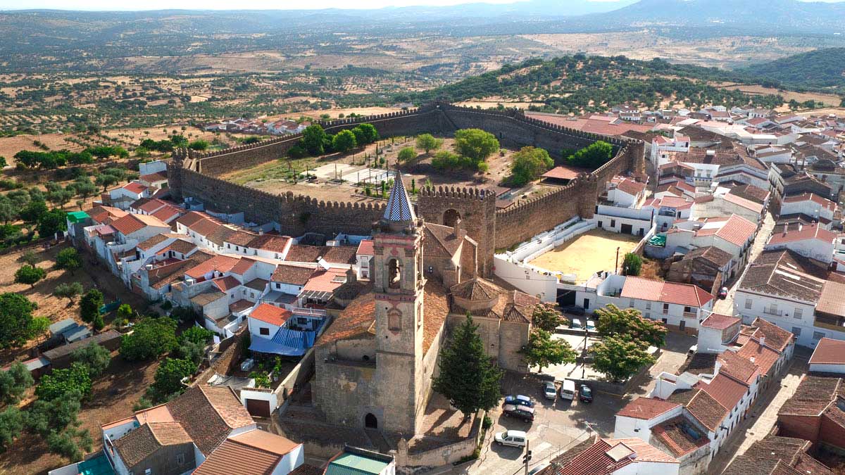 Vista aérea de Cumbres Mayores con su castillo medieval rodeado de dehesas en la Sierra de Huelva