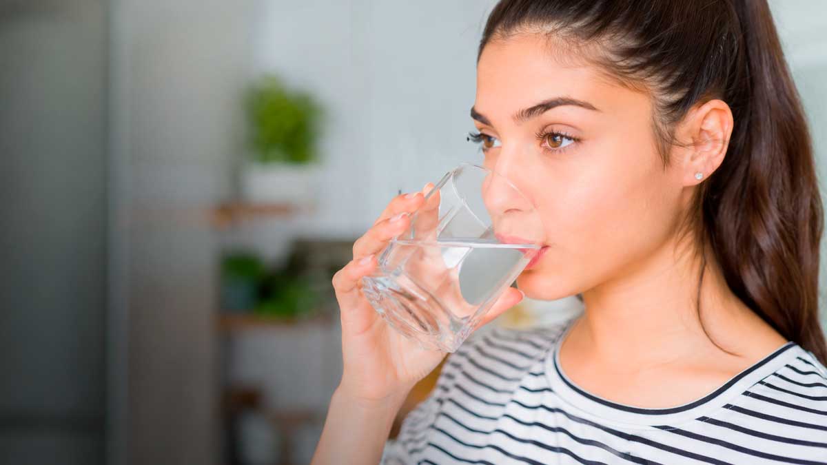 Mujer bebiendo agua en casa tras un estudio japonés sobre hidratación diaria