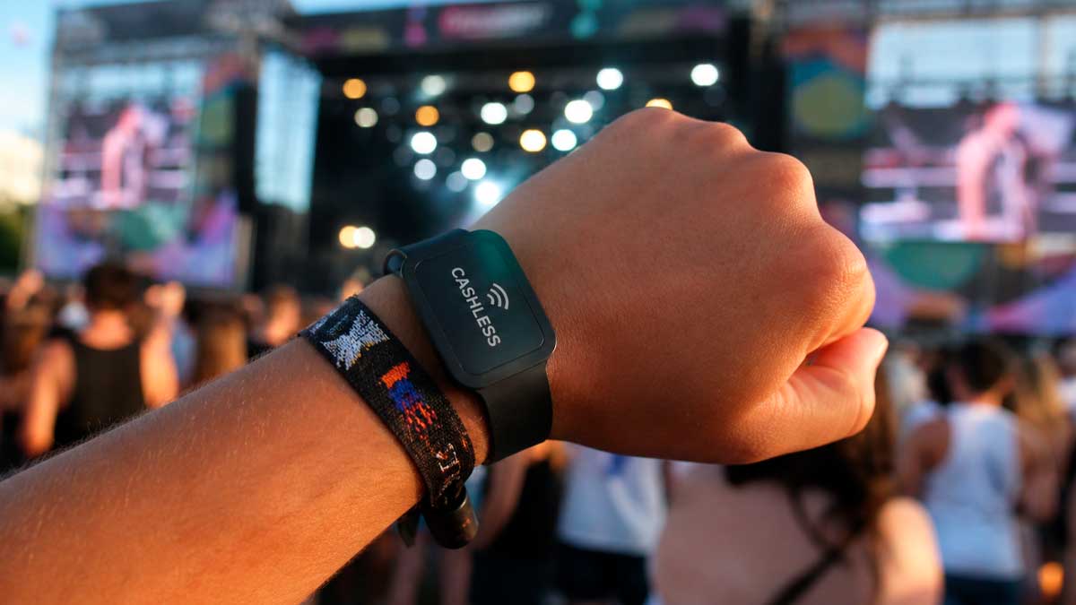 Pulsera cashless en festival de música con público y escenario al fondo en verano
