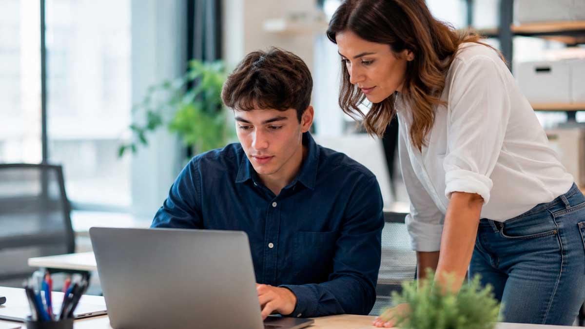 Trabajadora formando a un joven empleado con contrato de formación en alternancia en una oficina
