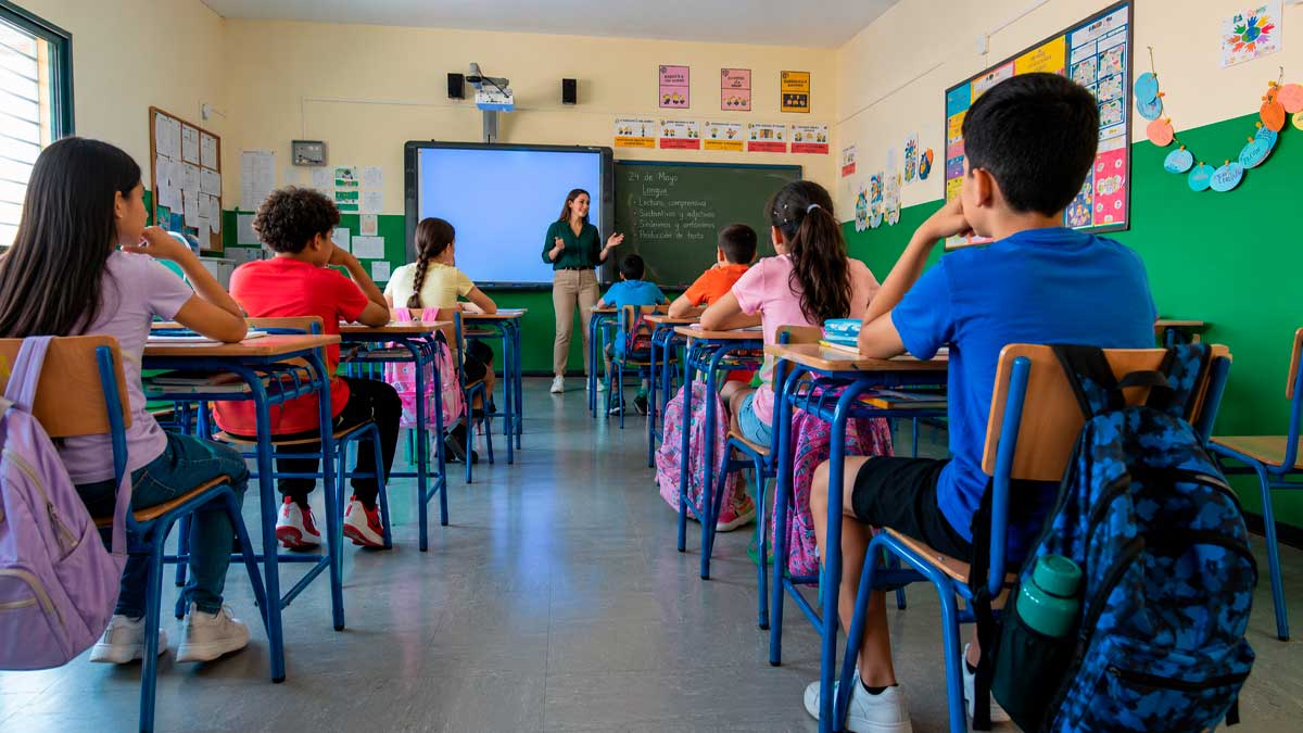 Aula de colegio en zona desfavorecida con alumnos y profesora, refuerzo docente en Andalucía