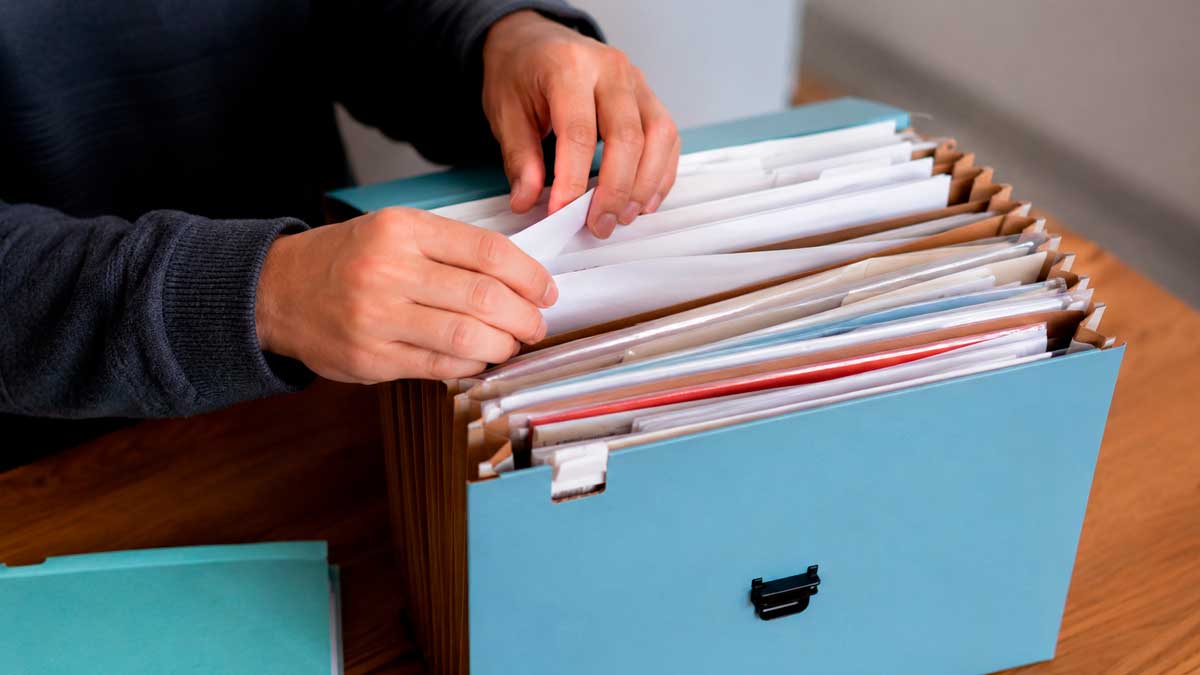 Persona organizando documentos importantes en una carpeta archivadora en casa