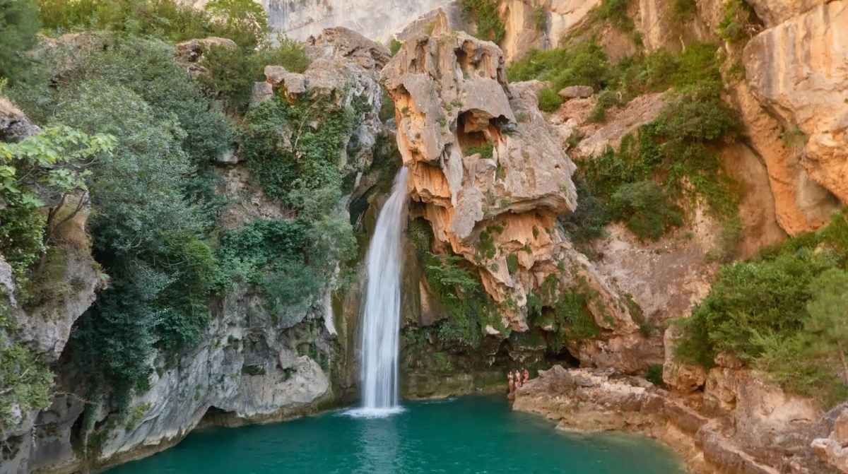 Cascada y poza de aguas turquesas en una piscina natural de Jaén rodeada de roca y vegetación