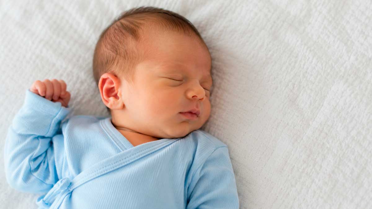 Bebé recién nacido vestido de azul descansando sobre una manta blanca en Andalucía