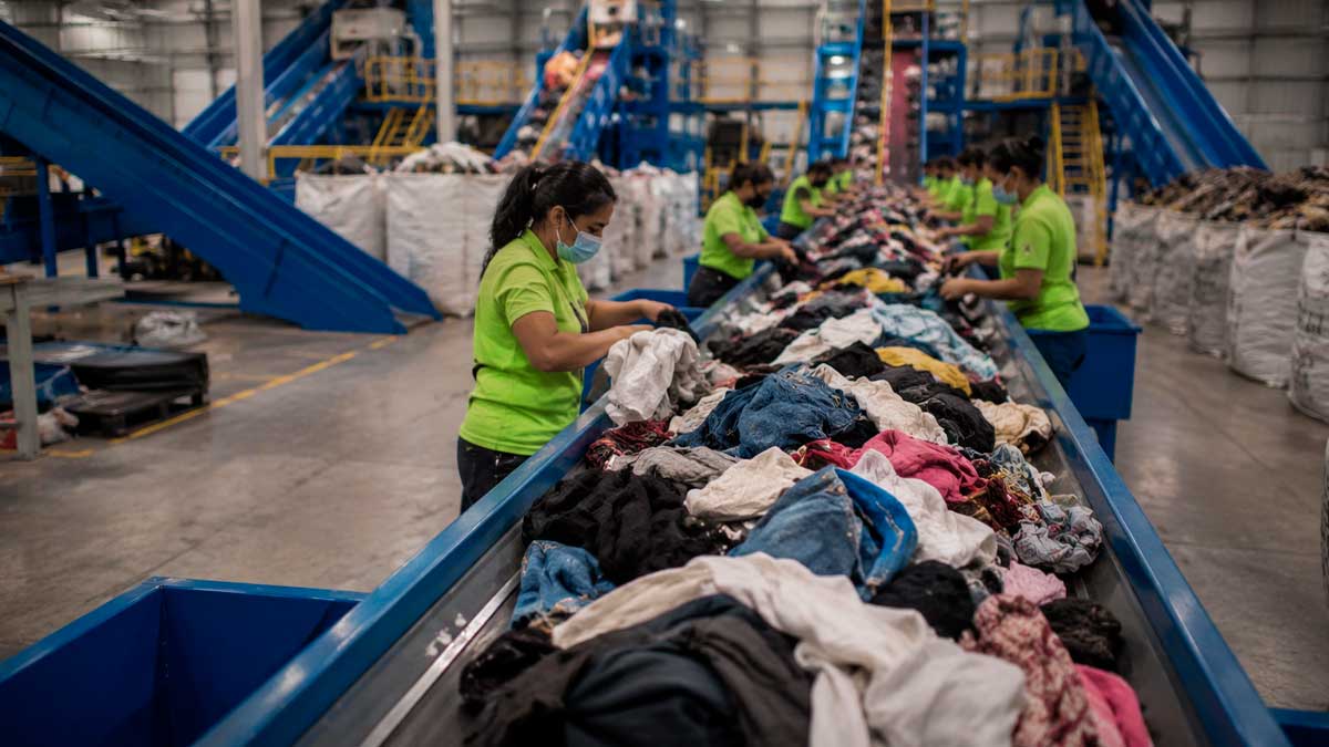 Operarios clasifican residuos textiles en una planta industrial de reciclaje con cintas transportadoras