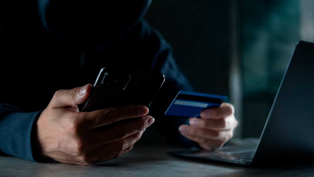 Persona utilizando un teléfono móvil y una tarjeta bancaria en una escena relacionada con el fraude por spoofing y el robo de datos