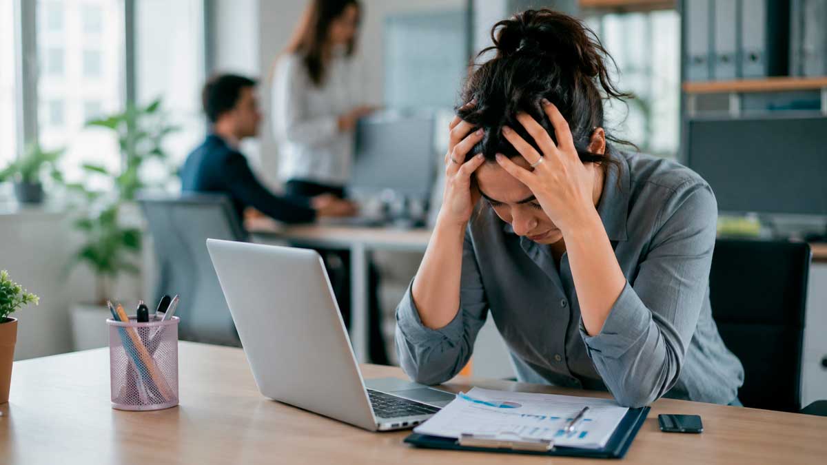 Absentismo laboral en Andalucía: mujer estresada en oficina frente a portátil